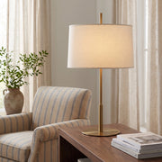 Novara Table Lamp in Lacquered Burnished Brass beside an armchair